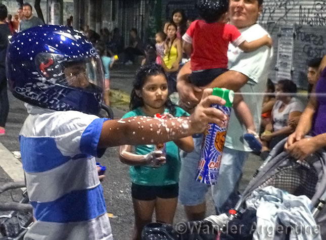 A child with a motorcycle helmet sprays foam from a can on the streets of Buenos Aires during Carnival celebrations