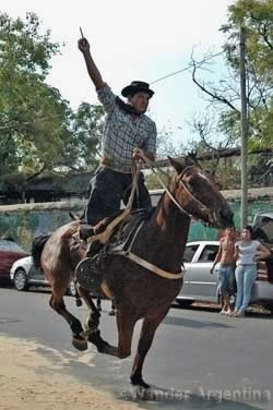 An Argentine cowboy on a horse holds up the ring he won in the corrida de sortijas