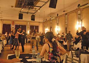 A woman looks on as couples embraced on the dance floor dance tango in a milonga, or tango dancehall of Buenos Aires 