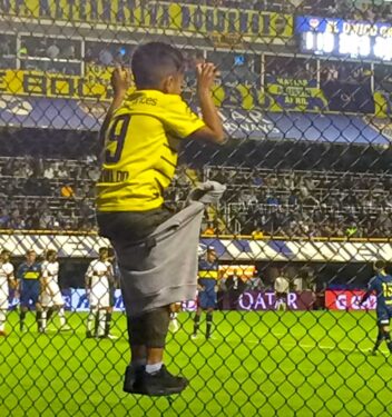 A child Boca Jrs fan on the fence watching the game